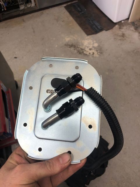 1992 Jeep Wrangler - A person's hand holds a metal fuel pump sending unit with two black AN fittings and a black corrugated hose attached. The sending unit is s…