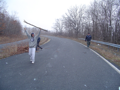 guy holding stick over head, another guy walking on road, snowy day