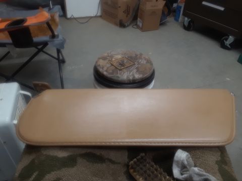 1994 Ford Bronco - A tan sun visor is laid out on a camouflage rug, with a brush and cloth nearby. The sun visor appears to be from a 1994 Ford Bronco.