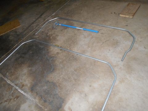 1992 Ford Bronco - Two bent metal tubes are laid out on a concrete floor. A blue pipe is placed on top of one of the tubes.