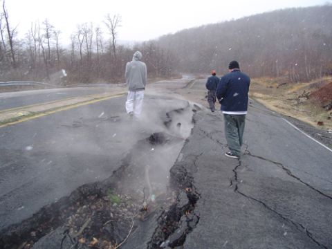 1979 Ford Bronco - A damaged road with large cracks and debris, with three individuals observing the scene in snowy weather.