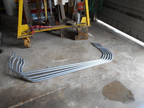 1992 Ford Bronco - A collection of bent metal tubes are laid out on a concrete floor in front of a yellow gantry crane. The tubes are curved and appear to be…
