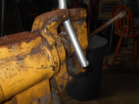 1992 Ford Bronco - A close-up shot shows a heavily rusted yellow vice holding a silver metal pipe. The background is dark and out of focus, with a wooden chai…
