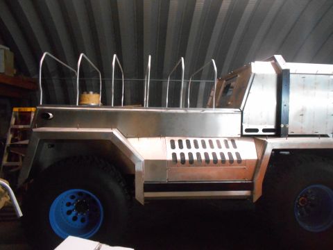 1992 Ford Bronco - A custom-built, heavy-duty vehicle with a brushed metal body is shown in a workshop setting. The vehicle features large off-road tires with…