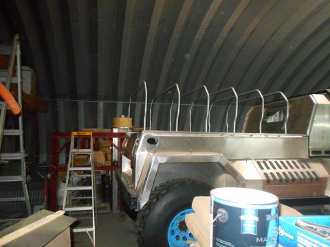 1992 Ford Bronco - A custom-built vehicle with a polished metal body sits in a workshop with a corrugated metal ceiling. Visible parts include a large tire wi…
