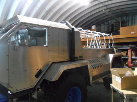 1992 Ford Bronco - The side view of a custom-built, unfinished vehicle with a brushed metal exterior is shown in a workshop setting. The vehicle features a la…