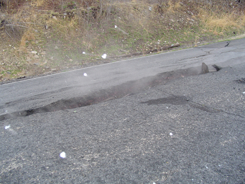 Cracked asphalt road with a large sinkhole on the side