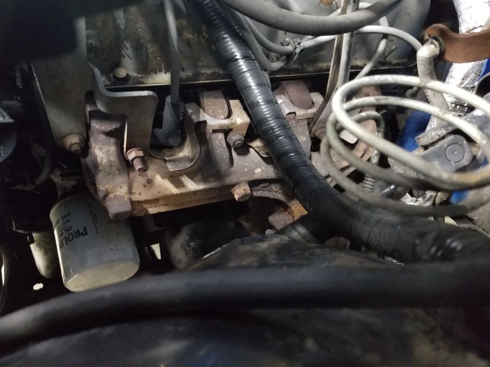 Engine bay close-up showing rusty exhaust manifold, white oil filter, wiring and hoses on a 1989 Ford Bronco.