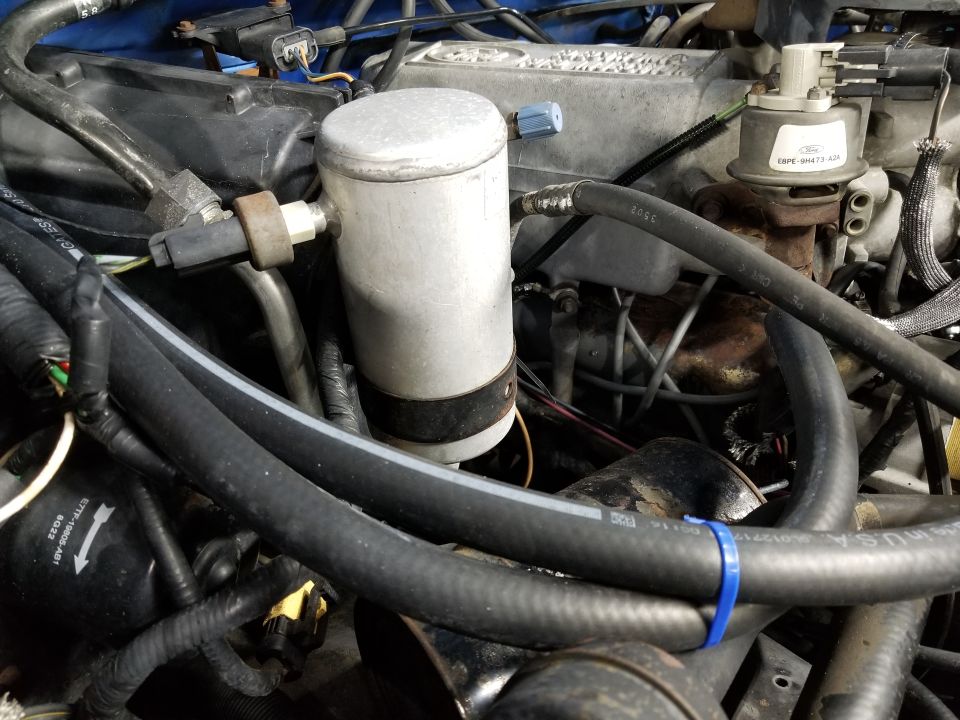 Close-up of an engine bay showing an AC accumulator, hoses, and wiring. Text on a hose reads 'USA'