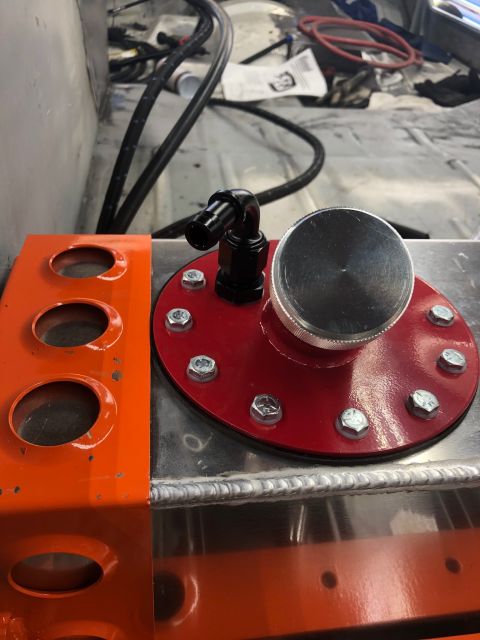 1992 Jeep Wrangler - A close-up view of a fuel tank cap and a black elbow fitting attached to a red plate, bolted onto a silver aluminum fuel tank. An orange me…