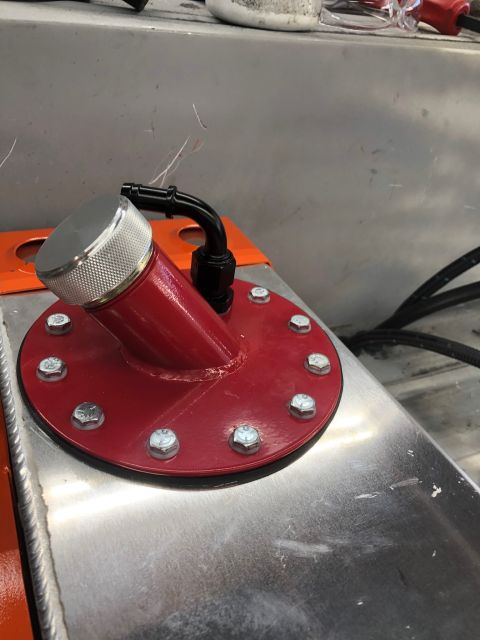1992 Jeep Wrangler - A close-up view of a red fuel cell cap assembly bolted to a brushed aluminum fuel tank. A black hose fitting is attached to the angled red…