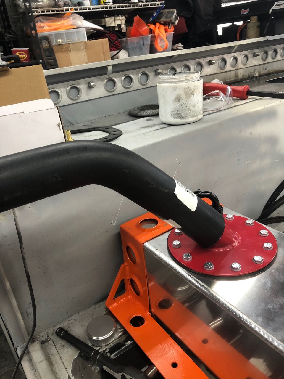 Black hose connected to a red fuel cell cap on a silver fuel tank with an orange bracket.