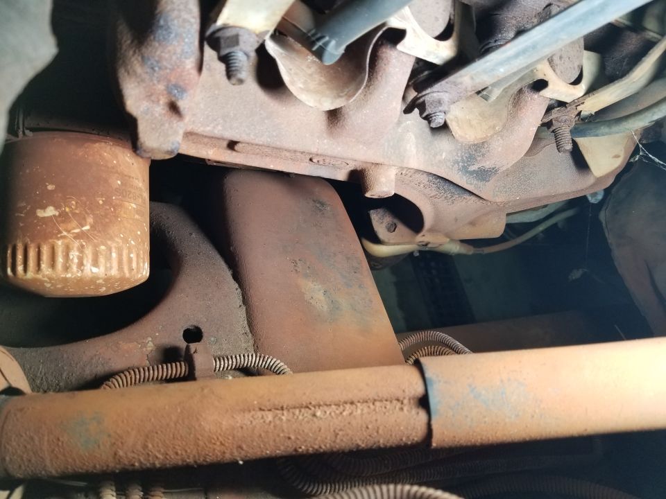 Close-up of rusted engine components including oil filter and exhaust manifold in a 1996 Ford Bronco.