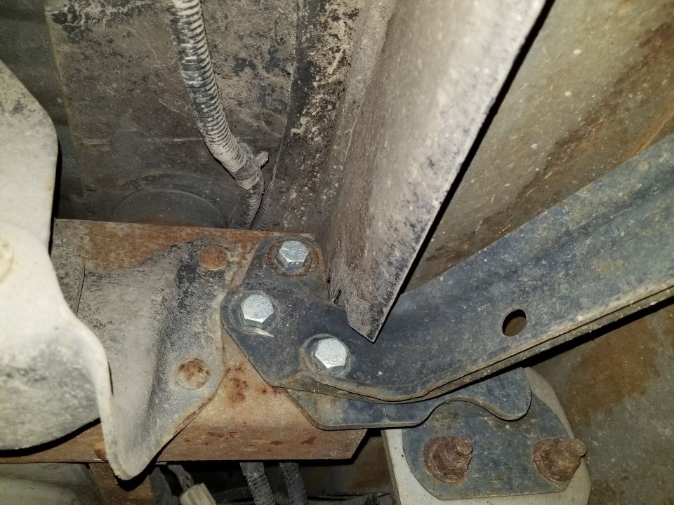 Underside of a vehicle showing a rusty frame bracket bolted with three new hex bolts near a body mount.