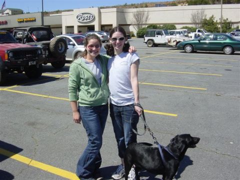 1995 Ford Bronco - Two people pose with a black Labrador on a leash in a shopping-center parking lot in front of a Roses store, with a red Jeep Cherokee, a wh…