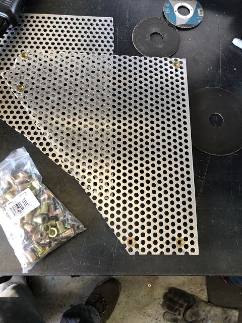 1992 Jeep Wrangler - A bag of brass-colored rivet nuts sits next to a piece of perforated metal sheeting on a black surface. Two grinding discs are also visible…