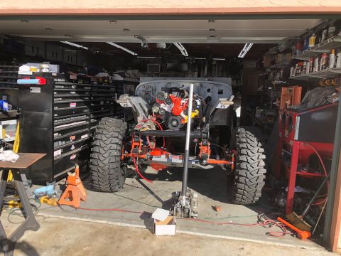 1992 Jeep Wrangler - A Jeep Wrangler is partially assembled in a garage, with its engine exposed and large off-road tires mounted. The vehicle is supported by a…