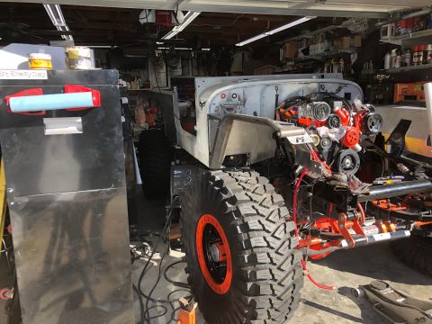 1992 Jeep Wrangler - A partially assembled Jeep Wrangler is in a garage, showing its engine, large off-road tires, and suspension components. A black tool chest…