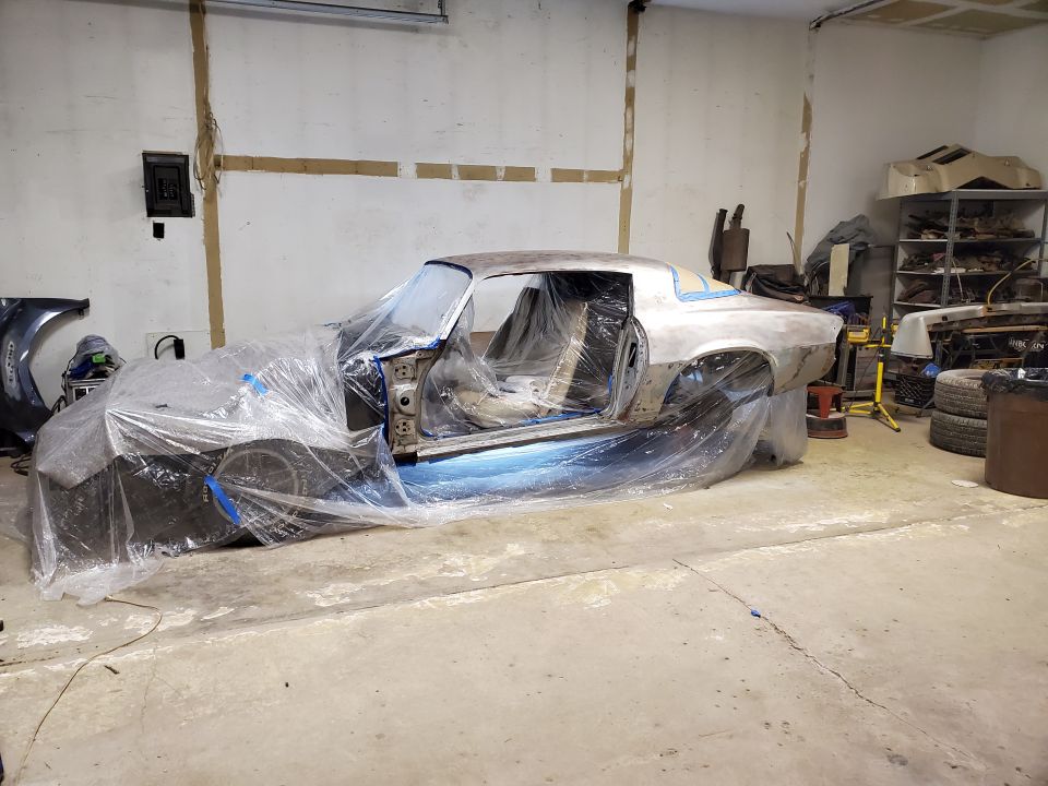1979 Chevrolet Camaro covered in plastic in a garage, bare metal body