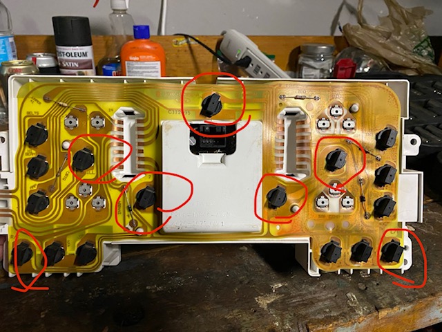 Back of a vehicle dashboard circuit board with black push-button switches circled in red.