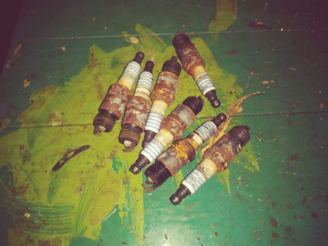 1996 Ford Bronco - A group of seven heavily rusted spark plugs are scattered on a green, paint-splattered surface.