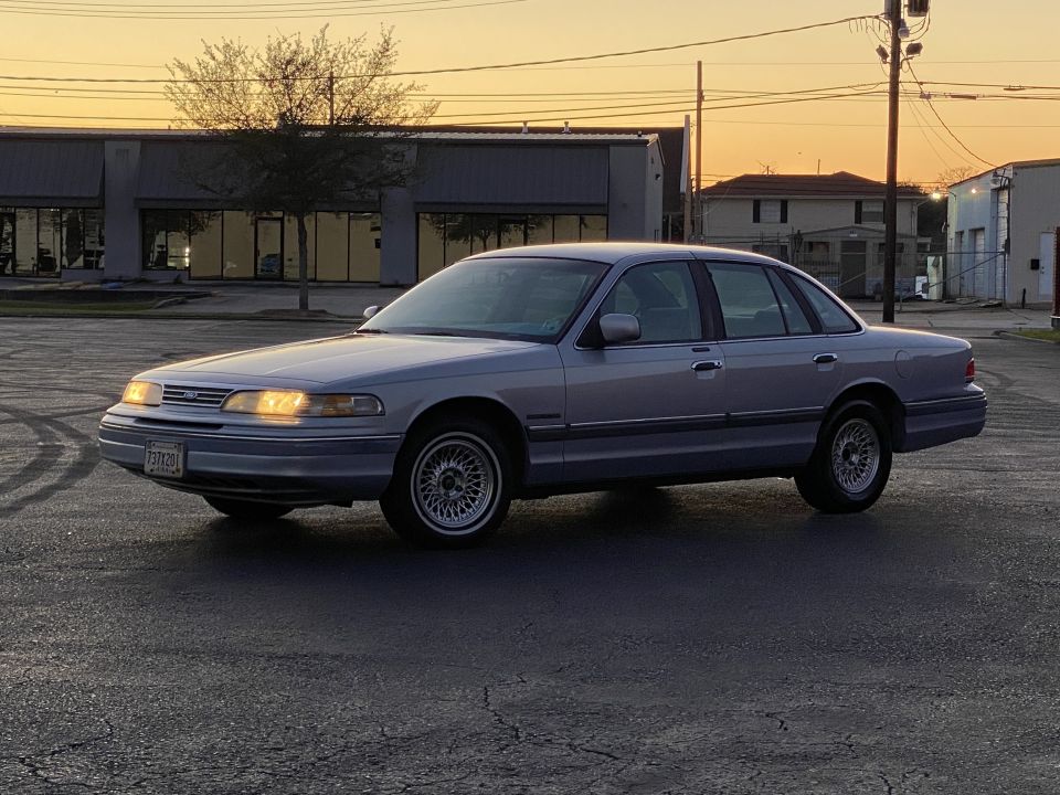 1994 Ford Crown Victoria sedan parked in an asphalt lot with headlights on.