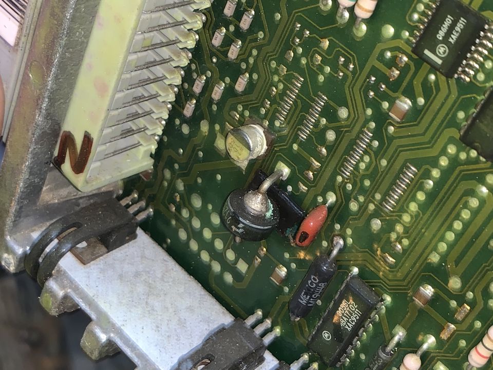 Close-up of green automotive PCB with capacitors, diodes, ICs and a white pin connector.
