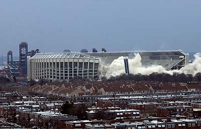 1979 Ford Bronco II - A stadium is being demolished, creating large dust clouds, with residential buildings and a clock tower visible.
