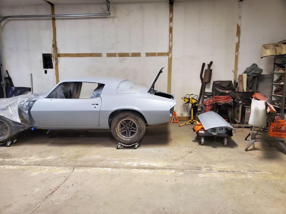 Light gray Chevrolet Camaro in a garage, partially covered, with hood and trunk open.