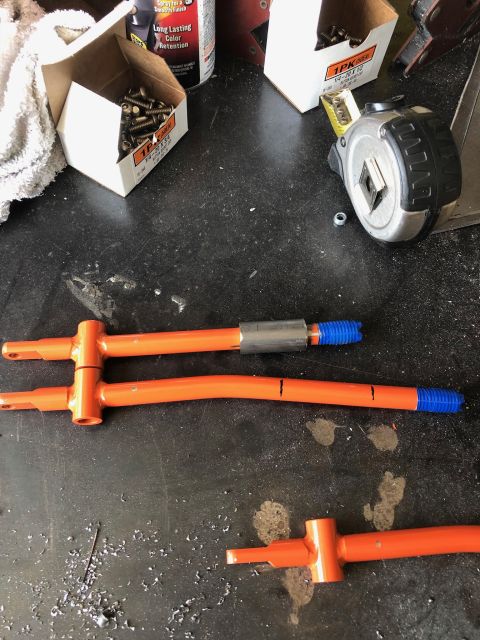 1992 Jeep Wrangler - pair of orange-painted sway bar end links or tie rods with threaded blue adjuster collars laid on a garage floor next to bolts and a spray…