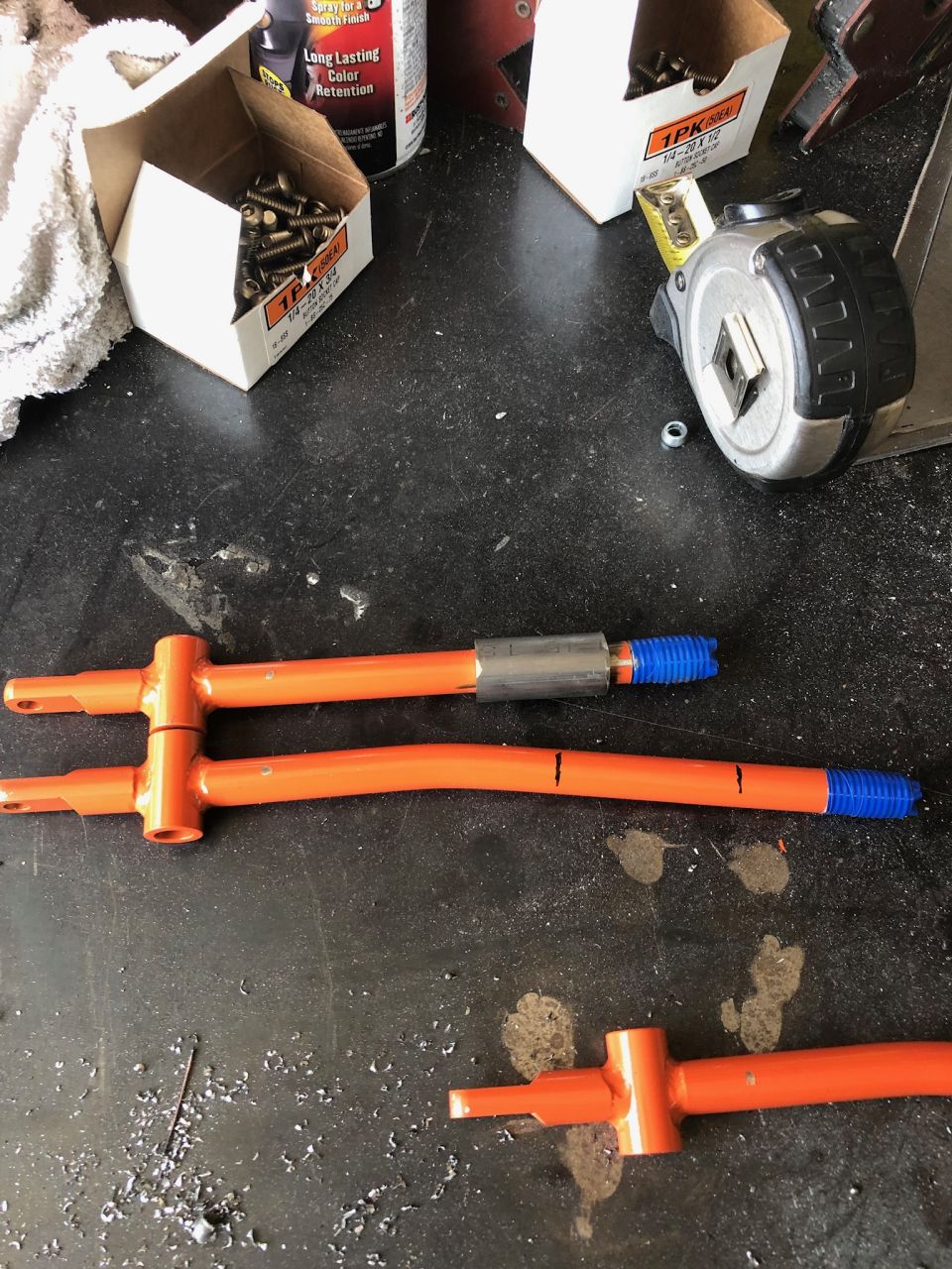 Two orange sway bar links or tie rod ends laid on a garage floor with boxes of hardware