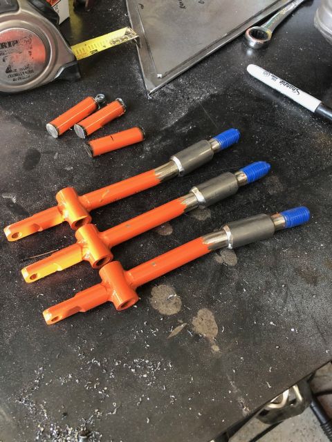 1992 Jeep Wrangler - Three orange painted metal parts with silver and blue ends are laid out on a dark, speckled workbench. Several smaller orange and silver cy…