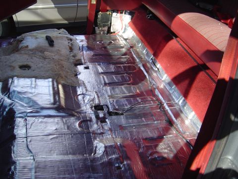 1986 Ford Bronco - Interior floor of a vehicle with reflective silver sound-deadening/insulation matting applied over the floor pan, with a red carpeted seat…