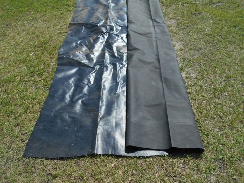 1992 Ford Bronco - Two large rolls of black plastic sheeting are laid out on a grassy area. The sheeting is partially unrolled, revealing a textured surface o…