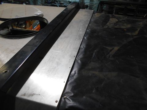 1992 Ford Bronco - A close-up view of a metal panel and black tarp covering part of a vehicle. A black metal bar runs along the edge of the metal panel.