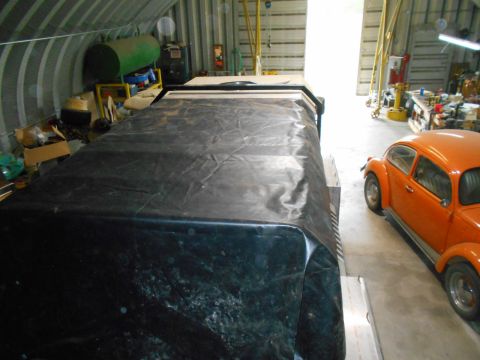1992 Ford Bronco - An orange classic Volkswagen Beetle is parked next to a large object covered in black tarp inside a garage or workshop. The Beetle is viewe…