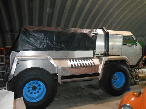 1992 Ford Bronco - A custom-built, heavy-duty truck with large tires and a silver aluminum body is parked inside a building with a corrugated metal roof. The…