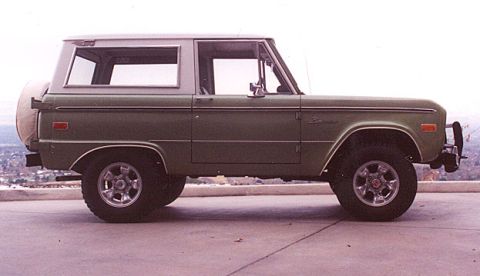 1973 Ford Bronco - Side view of a classic green Ford Bronco, its iconic body style and a spare tire mounted on the rear.