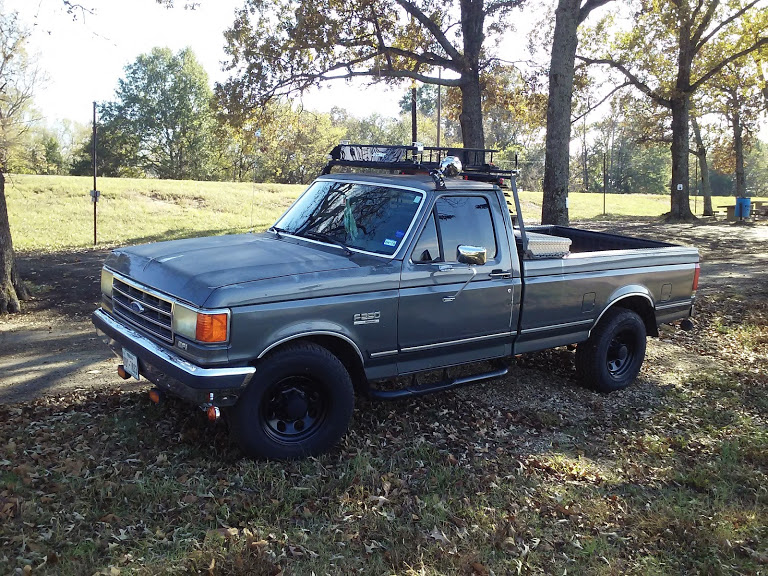 Gray Ford F-250 pickup truck with a roof rack and toolbox parked on a grassy area with trees