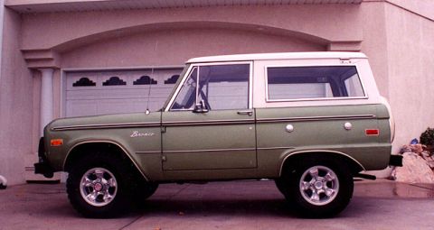 1973 Ford Bronco - A classic green 1973 Ford Bronco with a white hardtop is parked in front of a garage.