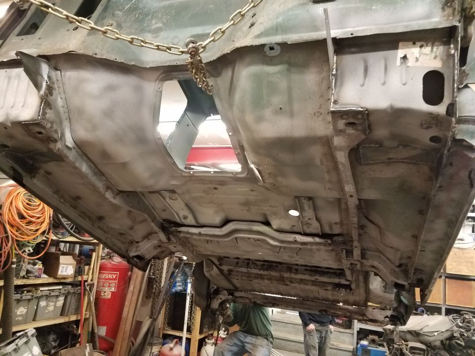 Underside of a vehicle suspended by chains, showing frame and floor pan.