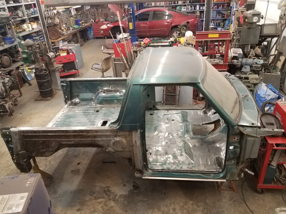 Disassembled green pickup truck cab and bed in a garage.