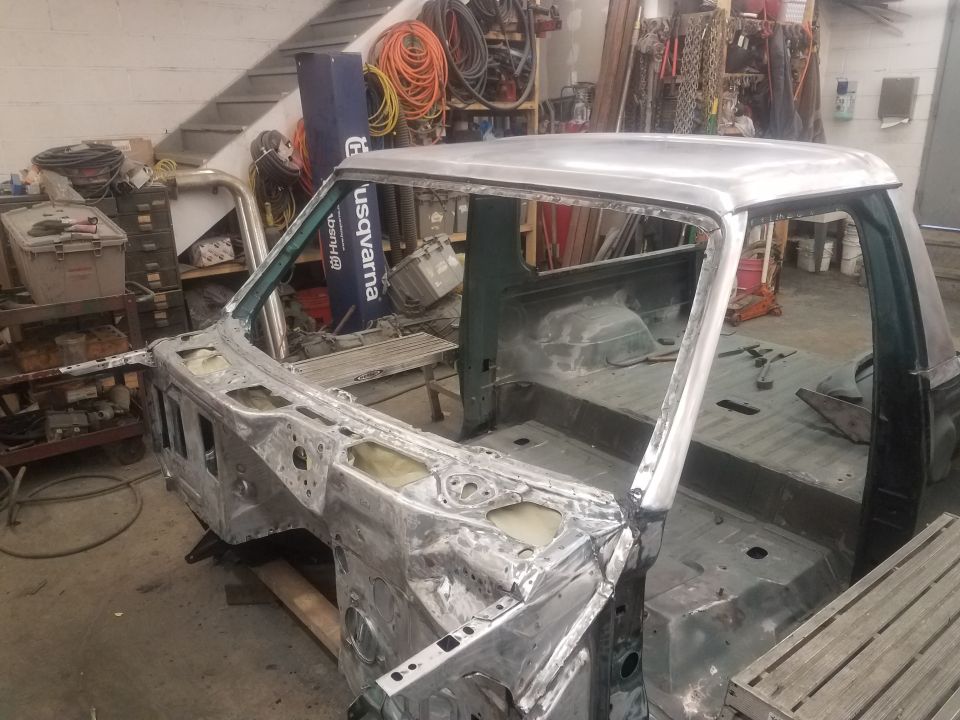 Bare metal pickup truck cab body in a workshop, undergoing restoration.