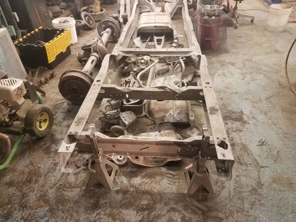 1994 Ford Bronco chassis on jack stands with engine and axles nearby.