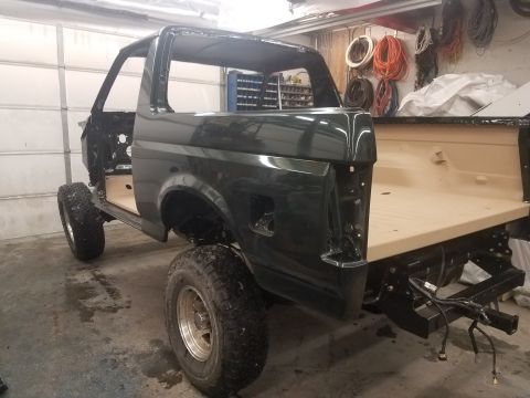 1994 Ford Bronco - A dark green 1994 Ford Bronco is shown in a garage during a restoration. The vehicle is missing its doors and interior, with the bed lined…