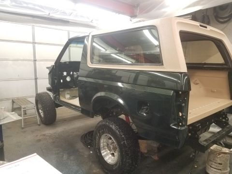 1994 Ford Bronco - A dark green Ford Bronco is shown from the side in a garage setting. The vehicle is undergoing restoration, with the doors removed and the…