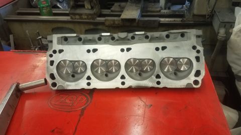 1994 Ford Bronco - A close-up, overhead view of a disassembled aluminum engine cylinder head with four sets of intake and exhaust valves visible. The cylinder…