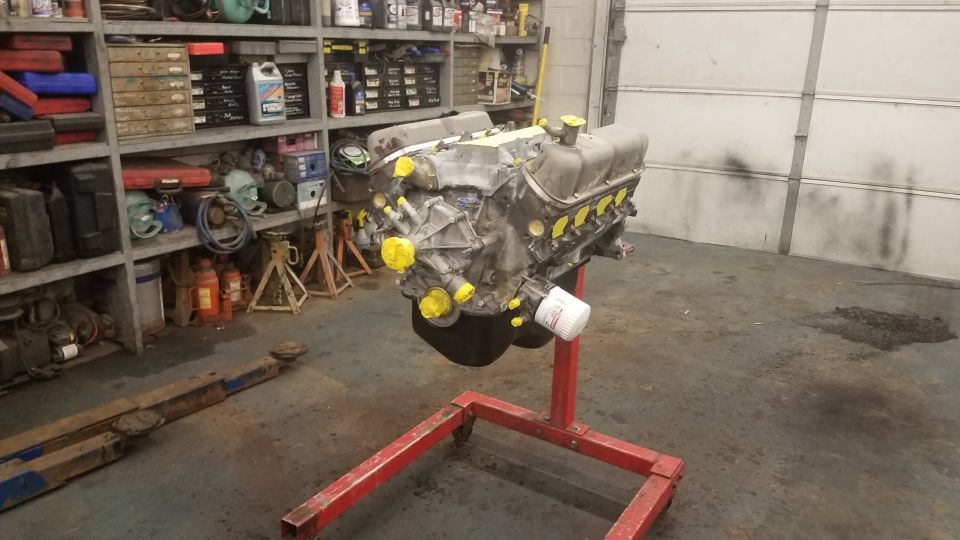 V8 engine on a red stand with yellow caps, garage setting.