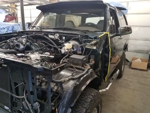 1994 Ford Bronco - This is a front 3/4 view of a dark green Ford Bronco undergoing some work in a garage. The hood and front fenders are removed, revealing th…