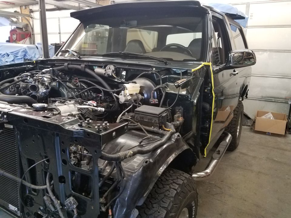 1994 Ford Bronco with front end disassembled in a garage.